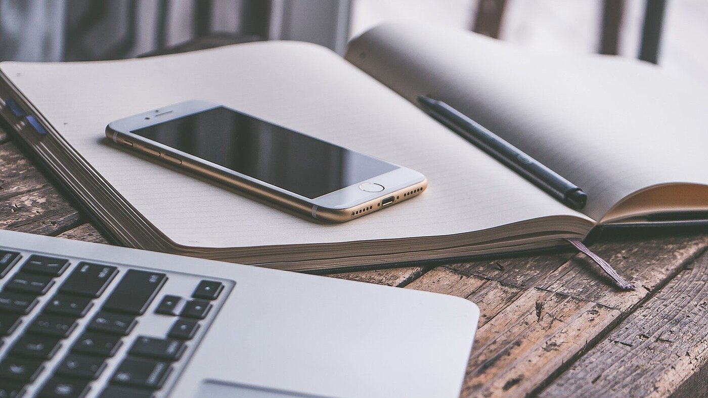 Freistellung Schreibtisch mit Laptop, aufgeschlagenem Notizbuch und Handy